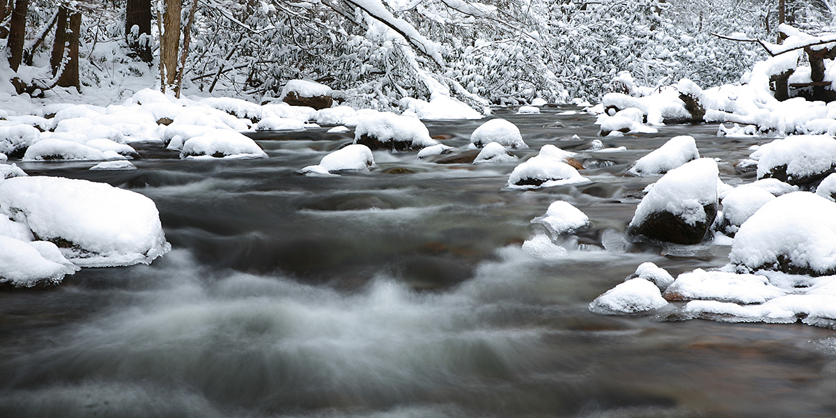 A stream flows over rocks covered in snow.